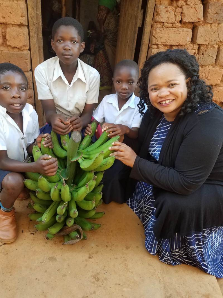 Julie sitting with three orphans and a big bunch of bananas.